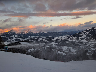 Obraz premium Snow-covered mountain landscape at sunset with a snow machine spraying snow on a ski slope