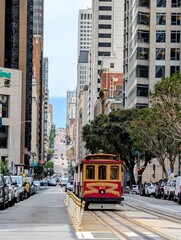 Fototapeta premium Iconic Cable Car Ascending a Steep San Francisco Street Lined with Tall Buildings and Parked Cars