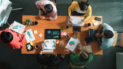 Top view of skilled businessman present marketing idea at meeting while group of investor listening and planning strategy while looking at stock market chart or data analysis document. Convocation.