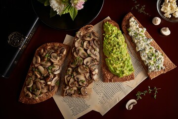 Four open-faced sandwiches are placed on a table featuring different toppings, revealing layers of mushrooms, avocado, and cheese