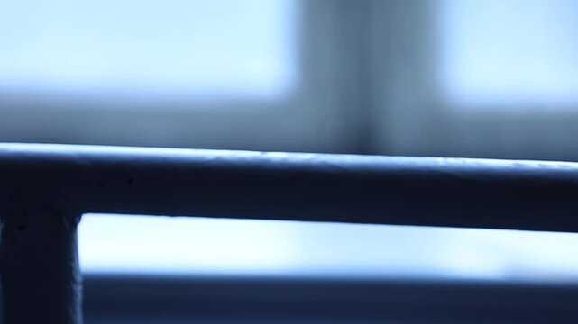 Cinematic close-up of a female dancer's hand gently gripping the ballet barre. A moody blue silhouette shot against a window in an empty dance studio during rehearsal.


