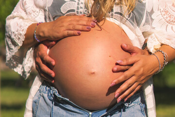 Primer plano de mujer embarazada y su pareja sosteniendo el vientre al aire libre bajo la luz del sol.