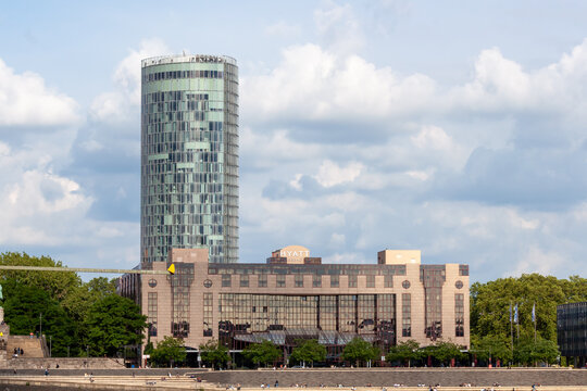 Modern skyline of Cologne, Germany, featuring the glass facade of KolnTriangle skyscraper, Hyatt Regency hotel, and the white arch of Zoobrucke bridge against a cloudy sky