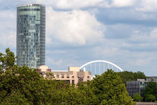 Modern skyline of Cologne, Germany, featuring the glass facade of KolnTriangle skyscraper, Hyatt Regency hotel, and the white arch of Zoobrucke bridge against a cloudy sky