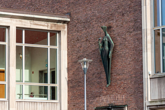 Bronze statue of a woman on a red brick wall of a public building in Cologne, Germany. Modernist architectural sculpture in the city center