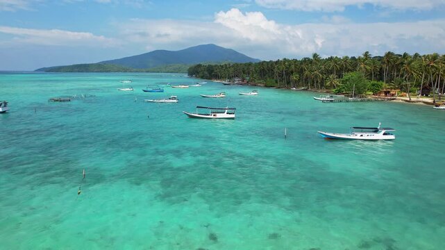 Aerial drone footage of local wooden fishing boats, in crystalline blue quiet waters , with beaches and forest, mountain behind, in Karimunjawa, island, Java island, Indonesia