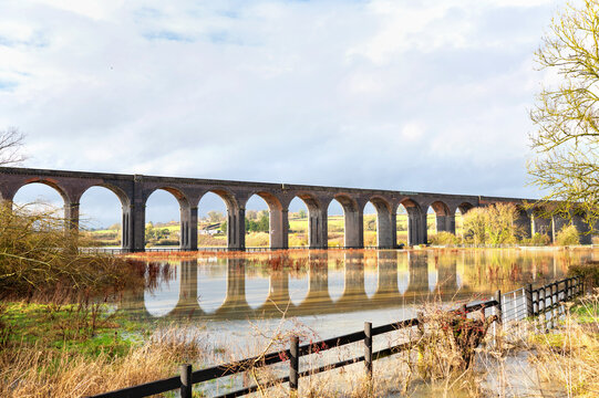 Large railway viaduct with multiple arches reflected in water near Harringworth, England.