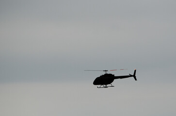 Single helicopter silhouetted against a pale gray sky