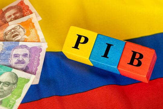 The word PIB Producto Interior Bruto (Gross Domestic Product) written on wooden cubes with colombian pesos money in yellow, lue and red flag of Colombia. Spain language