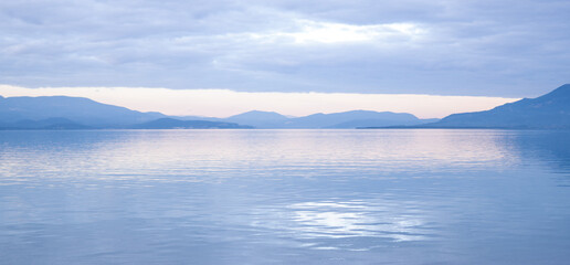 Calm sea bay panorama with mountain silhouettes at twilight or blue hour.