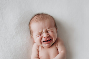 Crying newborn baby lying on white blanket.