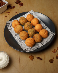 Top view of crispy fried croquettes on newspaper paper with dipping sauce and spices on wooden table