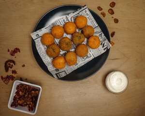 Top view of crispy fried croquettes on newspaper paper with dipping sauce and spices on wooden table