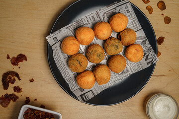 Top view of crispy fried croquettes on newspaper paper with dipping sauce and spices on wooden table