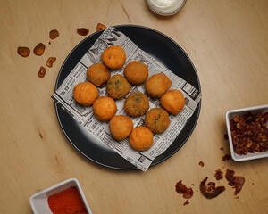 Top view of crispy fried croquettes on newspaper paper with dipping sauce and spices on wooden table