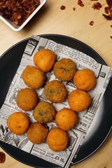 Top view of crispy fried croquettes on newspaper paper with dipping sauce and spices on wooden table
