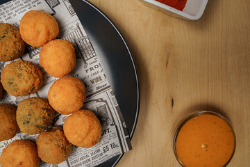 Top view of crispy fried croquettes on newspaper paper with dipping sauce and spices on wooden table