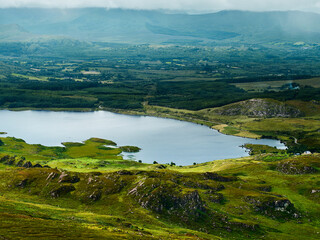 Viewing peaceful Lough and green countryside from rocky hillside during daytime.