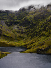 Lake nestled in a lush green valley with a cascade in National Park, on a cloudy day.