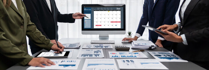 Panorama shot analyst team utilizing BI Fintech to analyze financial report with laptop. Businesspeople analyzing BI data dashboard displayed on laptop screen for business insight. Prodigy