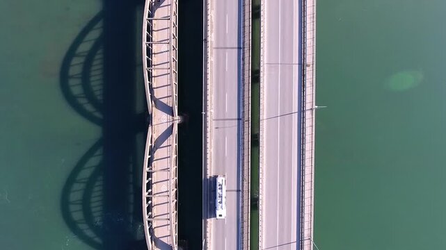 Aerial view shows old concrete arch bridge beside new highway bridge crossing river. Parallel transport structures highlight historic and modern engineering across flowing water.