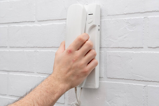 A man's hand lifts a white intercom telephone