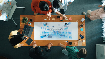 A group of professionals engage in a collaborative meeting, analyzing data visualizations and charts on a large table in a modern office environment. Trope