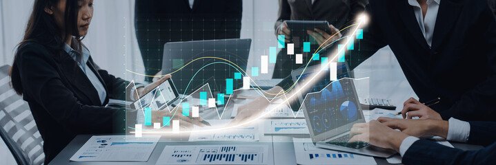 Business professionals engage in a collaborative meeting, analyzing financial data and graphs on laptops and tablets, highlighting strategies for growth and success. Axiom