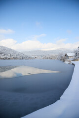 Obraz premium A calm winter landscape on the lake in the village of Semigorsky in the mountains of the city of Novorossiysk, snow-covered shores, the silence of nature and a cold atmosphere.