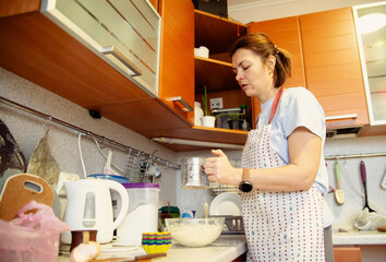 Woman in an apron sifting flour into a bowl to prepare dough in a cozy home kitchen. Capturing the essence of homemade baking and culinary tradition, ideal for food blogs, recipe features, and lifesty