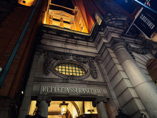 Naklejka premium Manchester clock tower building exterior at night with ornate entrance and Refuge Assurance Co signage