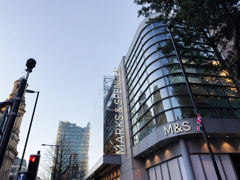 Marks and Spencer storefront in Manchester city center with modern glass building and Union Jack flag
