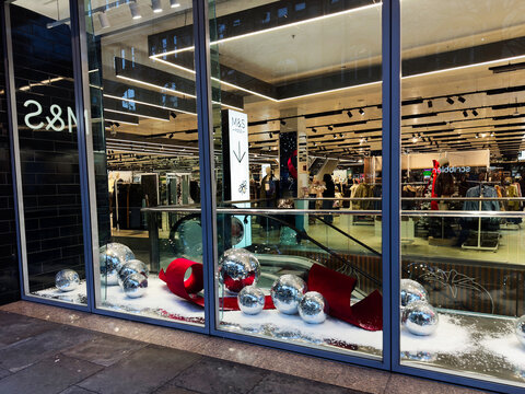 Shop window Marks and Spencer display with festive decor and shoppers inside a Manchester store UK
