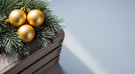 Three golden baubles rest on frosted fir branch inside a rustic wooden crate, representing festive decoration, seasonal spirit, and winter holiday
