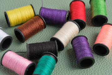 Spools of multicolored sewing threads on green leather background.