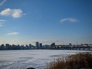 Winter cityscape of Dnipro, Ukraine with a long bridge over the frozen Dnipro River. Urban skyline under blue sky, cold weather landscape, travel and architecture concept.
