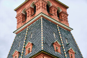 Close up historic Russian brick tower roof with green patterned tiles, arches, and decorative details against sky.