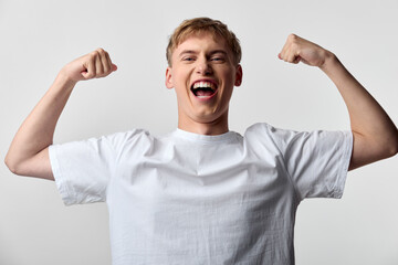 Celebration of success with a smiling, energetic male flexing arms in a white t shirt, conveying confidence and achievement, ideal for athletic, lifestyle, or motivational campaigns with dynamic