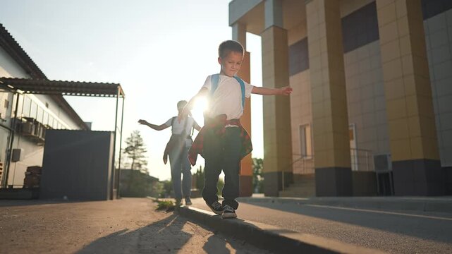 Playful student boy walks narrow curb near school entrance, arms spread for balance. Joyful walk becomes school play. Every student finds fun moment while walking carefully near morning class
