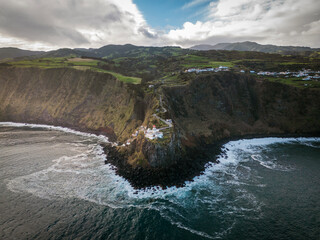Aerial vertical view of Arnel Lighthouse (Farol do Arnel) with steep winding road on a cliff at sunset, Sao Miguel, Azores.