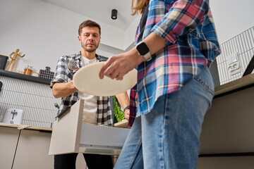 Man and woman standing in kitchen and unloading dishwasher with plates