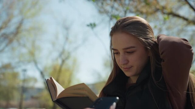 young woman reading, female student engrossed in book outdoors, youthful caucasian woman focused on reading in park sunshine, young female reader enjoying studying at sunny outdoor park bench