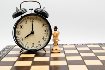 Alarm clock showing 8 o'clock and chess king on a chessboard symbolizing time management, strategy, leadership and decision making in business planning, deadlines and strategic thinking.