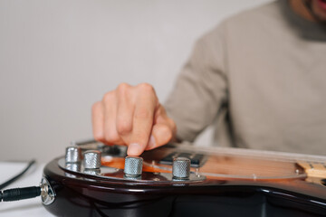 Close-up hands of musician adjusting sound, tone, volume on electric bass guitar with hand, preparing for performance or practice session in music studio or home setting, focusing on audio quality.