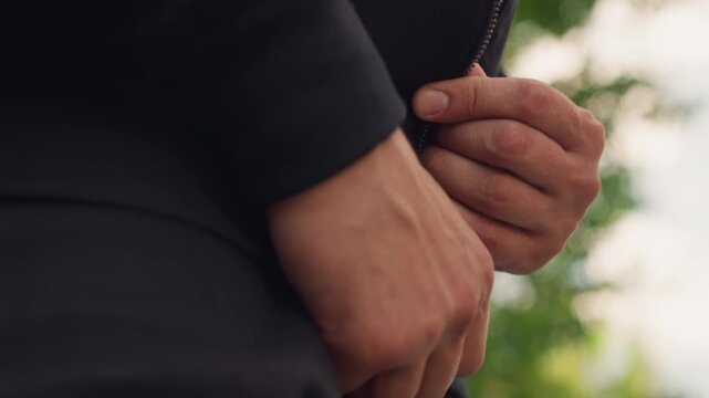 caucasian man prepares for outdoor walk outdoors, closeup of hands fixing drawstring with trees behind him, focused on hands adjusting clothing as man gets ready for outdoor adventure