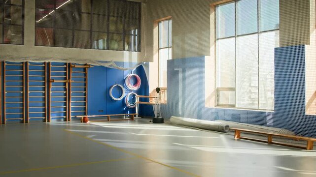 Wide angle shot of empty school gym with various sports equipment and protective netting on walls lit by sunlight, no people, copy space