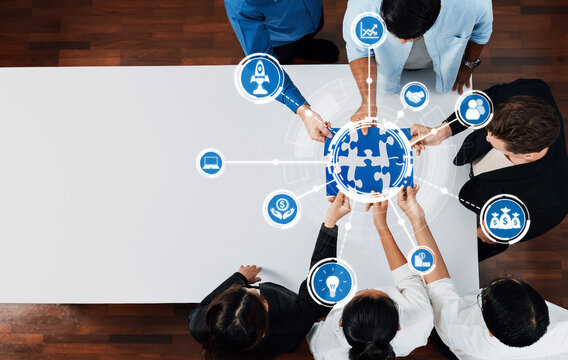 A diverse team collaborates to solve business challenges, holding a globe puzzle while utilizing digital icons for innovation and strategy in a modern workspace setting. Amity - Powered by Adobe