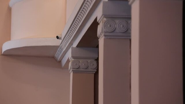 Close-up pan across intricate architectural details inside a classic building. The shot features white plaster moldings, arches, and columns against a warm, elegant peach-colored wall interior.

