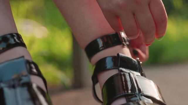 hand fastening sandal strap with painted nails on sunlit bench, close detail of buckle and glossy leather as foot prepares to walk; intimate styling and preparation captured in warm afternoon light