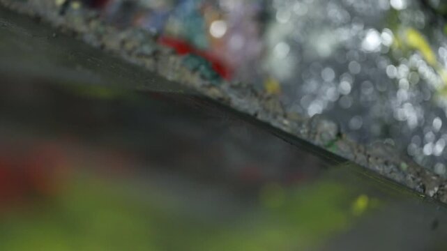 Close-up of artist's hand dipping paintbrush into solvent cup on colorful wooden palette. Detailed shot of creative painting process in art studio environment with oil paints.

